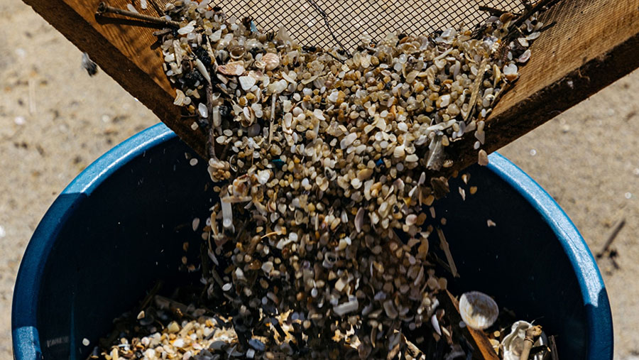 Pekerja kebersihan menyaring pasir untuk mengumpulkan plastik yang terdampar di pantai di Uswetakeiyawa, Sri Lanka. (Jonathan Wijayaratne/Bloomberg)