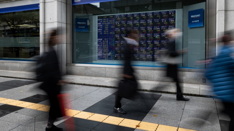 Para pekerja berjalan di depan papan layar perdagangan saham Asia (dok Bloomberg)