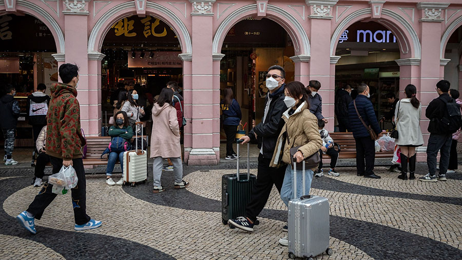 Pelancong membawa koper mereka di Leal Senado Square di Makau, China, Rabu (25/1/2023). (Eduardo Leal/Bloomberg)