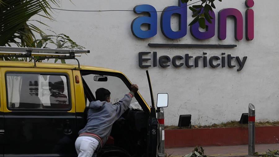 Warga mendorong mobil di depan logo Adani Group di Mumbai, India, Jumat (27/1/2023). (Indranil Aditya/Bloomberg)