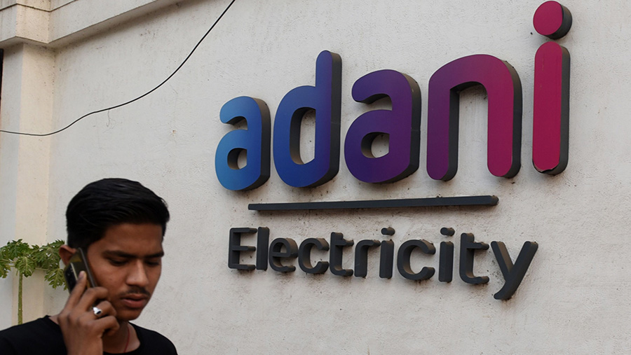 Warga beraktivitas di depan logo Adani Group di Mumbai, India, Jumat (27/1/2023). (Indranil Aditya/Bloomberg)