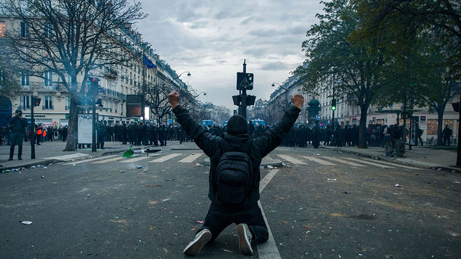 Pedemo berlutut di depan polisi anti huru hara selama aksi menentang reformasi pensiun di Paris, Prancis, Selasa (28/3/2023). (Nathan Laine/Bloomberg)