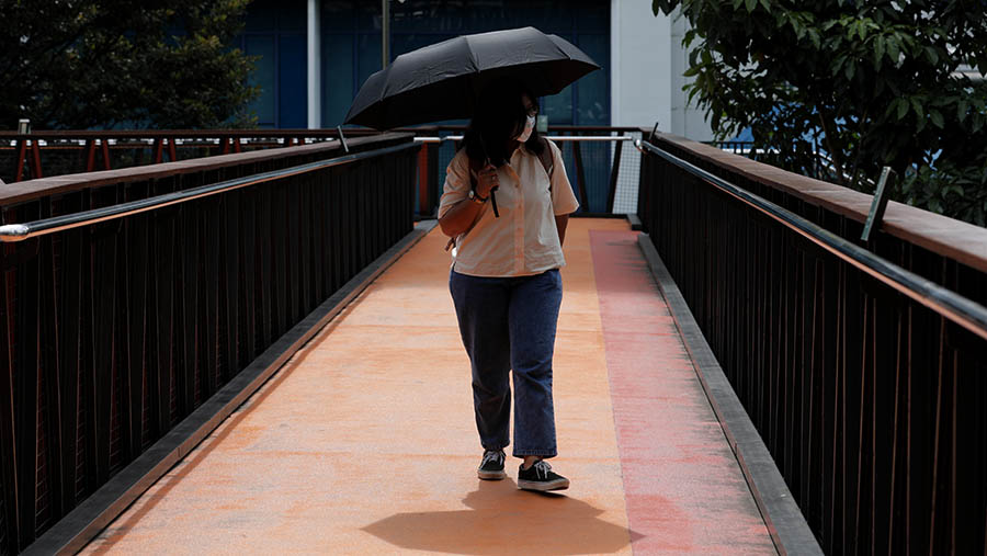 Warga menggunakan payung untuk menghalau panas di kawasan Sudirman, Jakarta, Kamis (13/4/2023). (Bloomberg Technoz/ Andrean Kristianto)