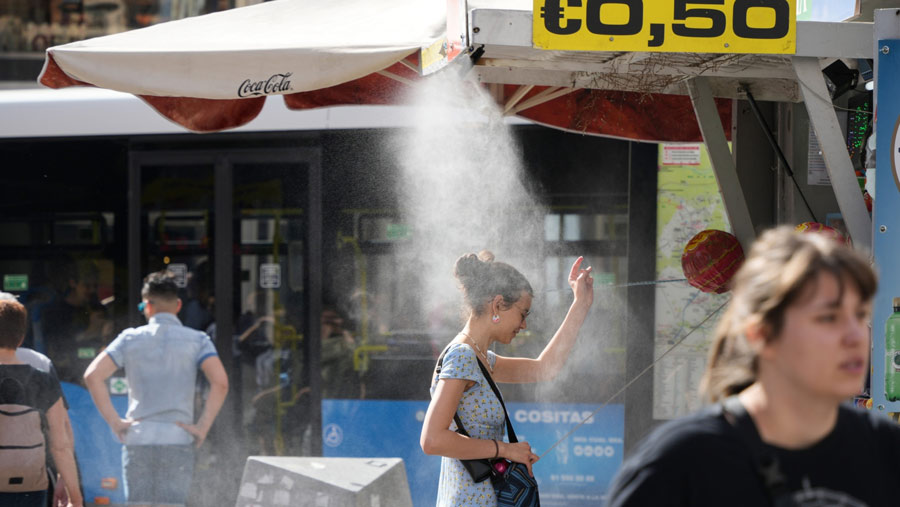 Seorang wanita berdiri di bawah semprotan kabut pendingin di sebuah kios selama suhu tinggi di Spanyol (Paul Hanna/Bloomberg)