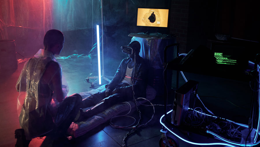 Pria Afrika duduk di lantai dengan kacamata VR di wajahnya sementara rekannya menghubungkannya dengan monitor komputer di ruangan gelap (Dok Envato)