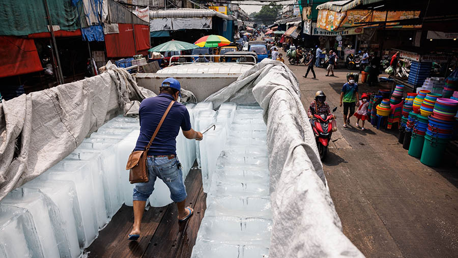 Seorang pekerja membelah balok es di pasar basah saat gelombang panas di Bangkok (27/4/2023). (Andre Malerba/Bloomberg)