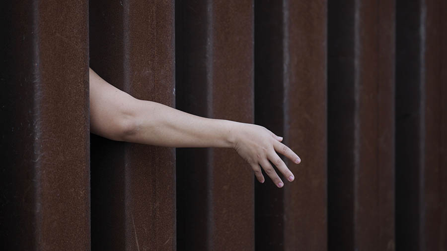 Seorang imigran mencapai pagar di perbatasan AS-Meksiko di San Diego, California, AS, Jumat (12/5/2023). (Eric Thayer/Bloomberg)