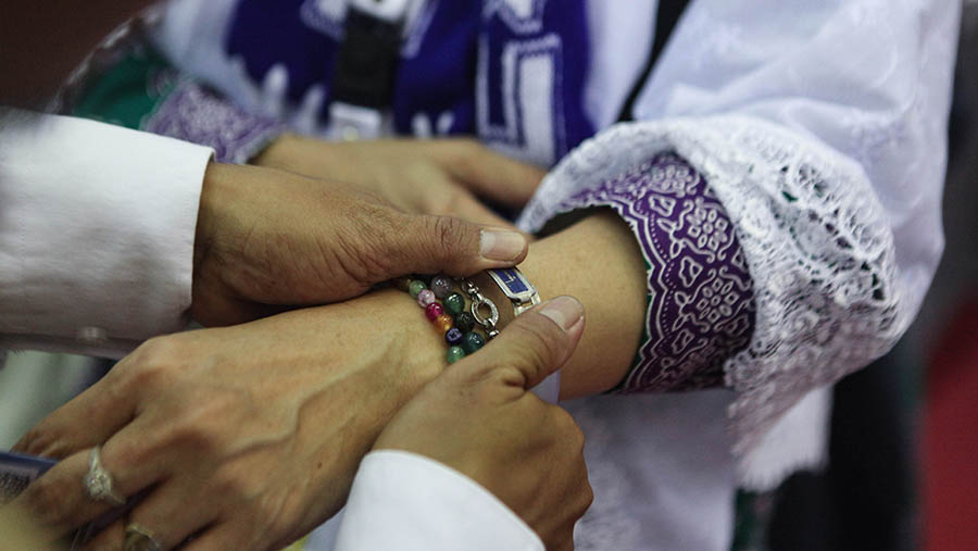 Petugas memasangkan gelang ke calon jemaah haji di Asrama Haji Pondok Gede. (Bloomberg Technoz/ Andrean Kristianto)