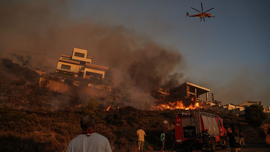 Petugas memadamkan gedung yang terbakar saat kebakaran hutan di Saronida, selatan Athena, Yunani, Senin (17/7/2023). (Nick Paleologos/Bloomberg)
