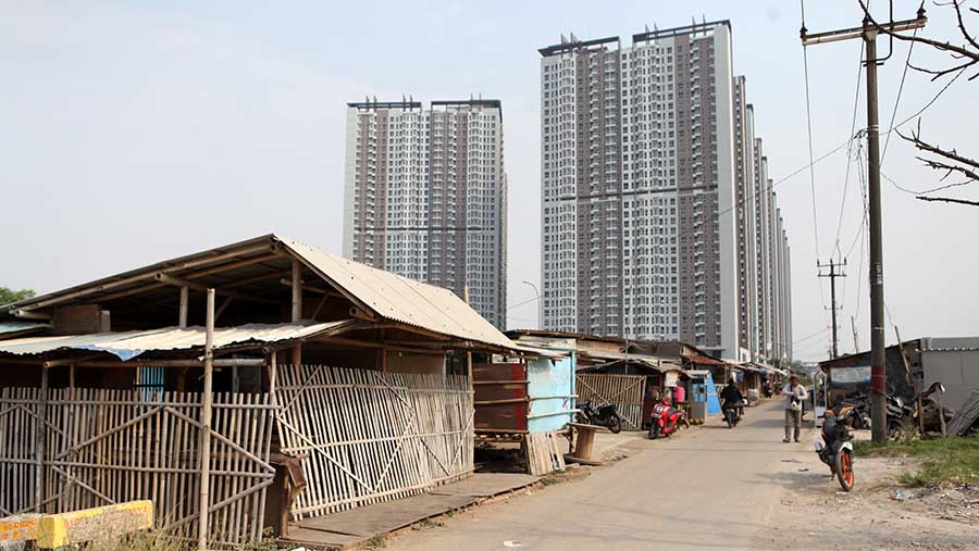 Warga melintas di Kampung Muara, Teluknaga, Tangerang, dengan latar apartemen, Rabu, (2/8/2023). (Bloomberg Technoz/ Andrean Kristianto)