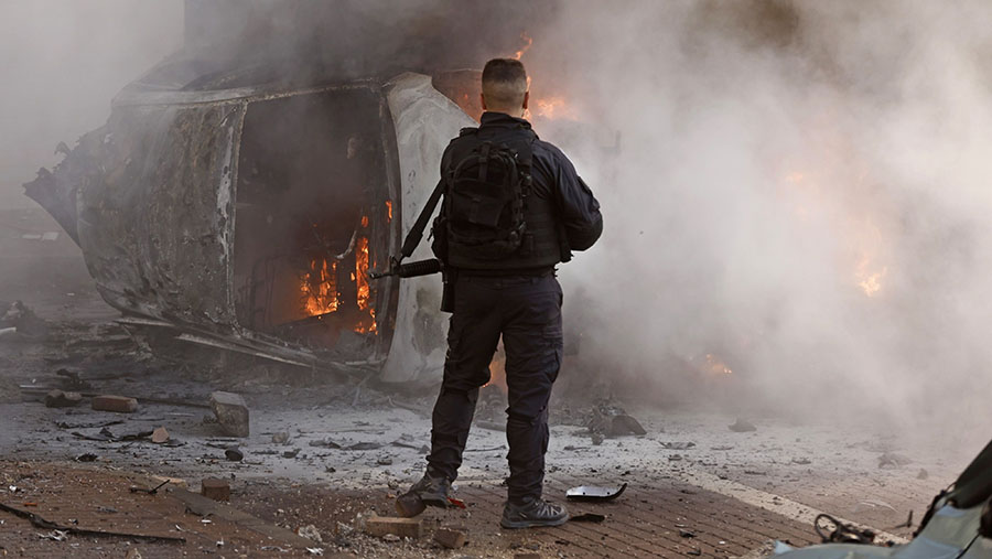 Anggota pasukan keamanan di samping mobil yang terbakar menyusul serangan roket Hamas di Ashkelon, Israel, Sabtu, (7/10/2023). (Kobi Wolf/Bloomberg)