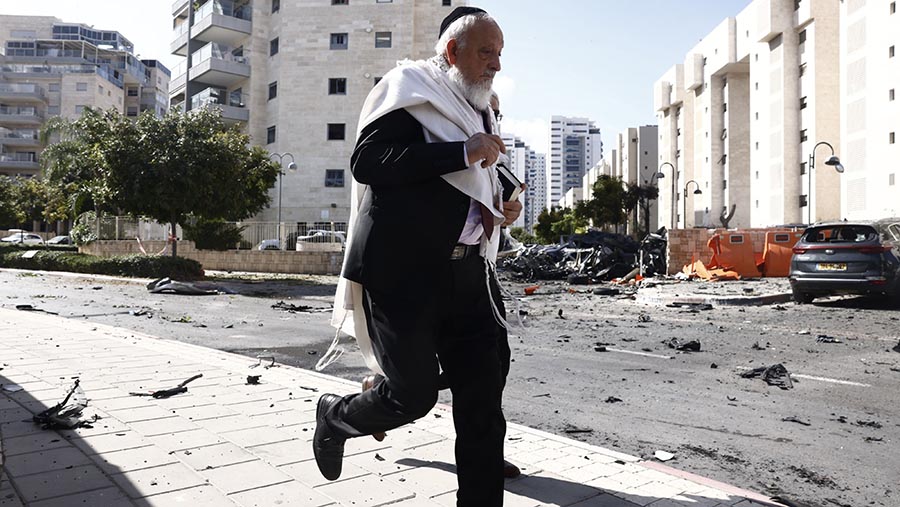 Seorang pria berlari melewati mobil yang rusak akibat serangan roket Hamas di Ashkelon, Israel, Sabtu, (7/10/2023). (Kobi Wolf/Bloomberg)