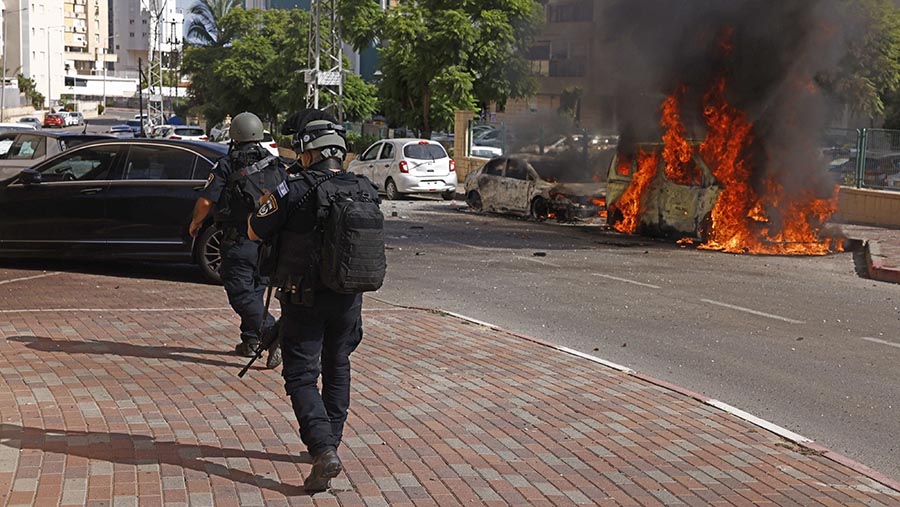 Pasukan keamanan melewati mobil yang terbakar menyusul serangan roket Hamas di Ashkelon, Israel, Sabtu, (7/10/2023). (Kobi Wolf/Bloomberg)