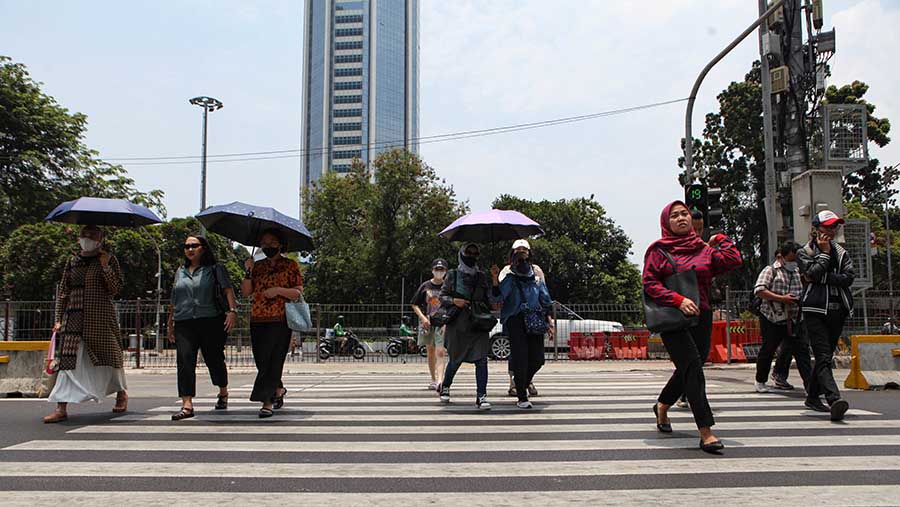 Warga menggunakan payung saat cuaca panas di Jakarta, Selasa (10/10/2023). (Bloomberg Technoz/Andrean Kristianto)