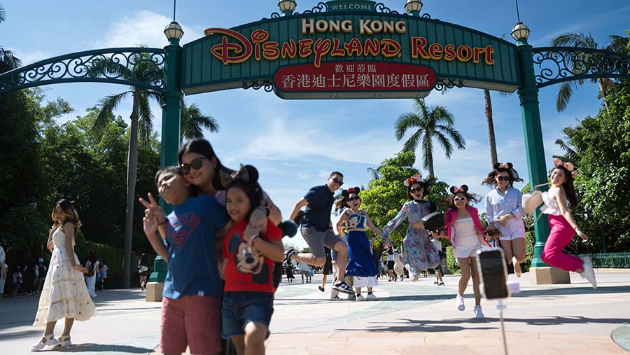 Pengunjung berpose di depan papan nama di Disneyland Resort Walt Disney Co. di Hong Kong, Jumat (13/10/2023). (Bertha Wang/Bloomberg)