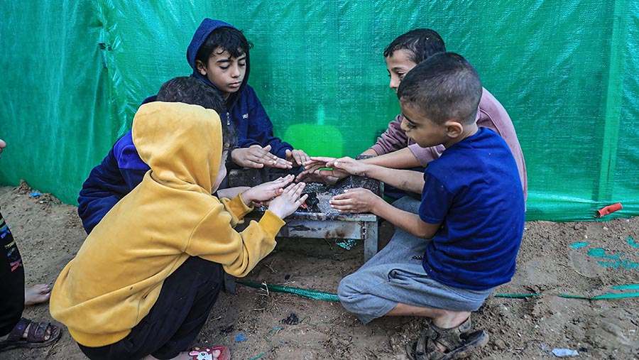 Anak-anak menghangatkan diri di kamp pengungsi dekat rumah sakit Shuhada Al-Aqsa, Gaza, Senin (13/11/2023). (Ahmad Salem/Bloomberg)