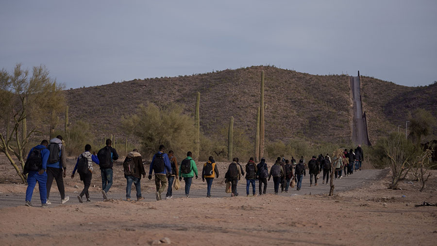 Para migran berjalan di sepanjang pagar perbatasan AS-Meksiko di Lukeville, Arizona, AS, Senin (11/12/2023). (Eric Thayer/Bloomberg)