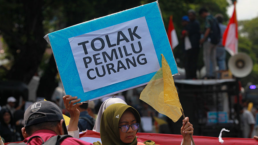 Peserta aksi memegang poster bertuliskan 'Tolak Pemilu Curang' saat demo di KPU Pusat, Senin (19/2/2024). (Bloomberg Technoz/Andrean Kristianto)