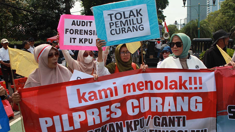 Peserta aksi memegang poster bertuliskan 'Tolak Pemilu Curang' saat demo di KPU Pusat, Senin (19/2/2024). (Bloomberg Technoz/Andrean Kristianto)