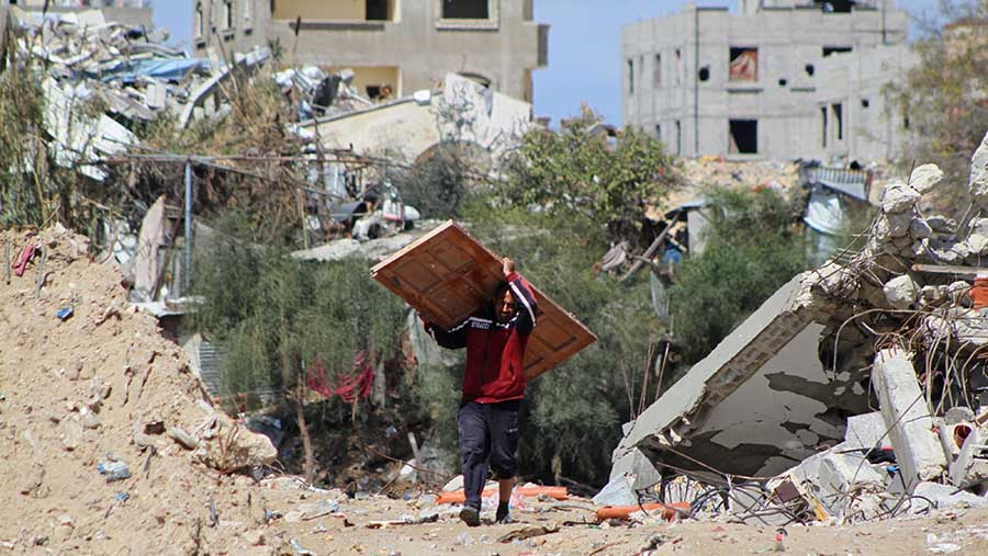Pria Palestina menyelamatkan pintu dari puing bangunan yang hancur usai serangan Israel di Khan Younis, Gaza (8/3/2024). (Ahmad Salem/Bloomberg)