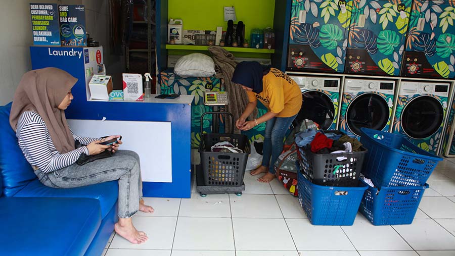 Pekerja menimbang pakaian kotor pelanggan di jasa pencucian pakaian di Pejaten, Jakarta, Selasa (6/4/2024). (Bloomberg Technoz/Andrean Kristianto)