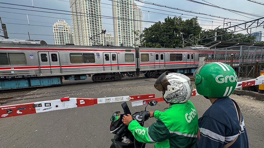 Driver ojol Grab berhenti diperlintasan KRL di dekat Stasiun Kebayoran Lama, Jakarta, Jumat (19/4/2024). (Bloomberg Technoz/Andran Kristianto)