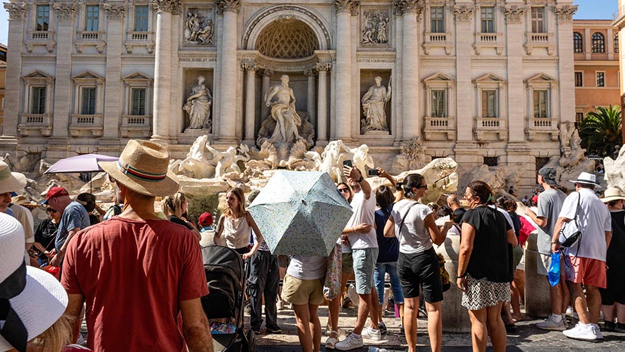Turis berlindung dari terik matahari dengan payung dan topi matahari di Roma, Italia, Sabtu (13/7/2024). (Stephanie Gengotti/Bloomberg)