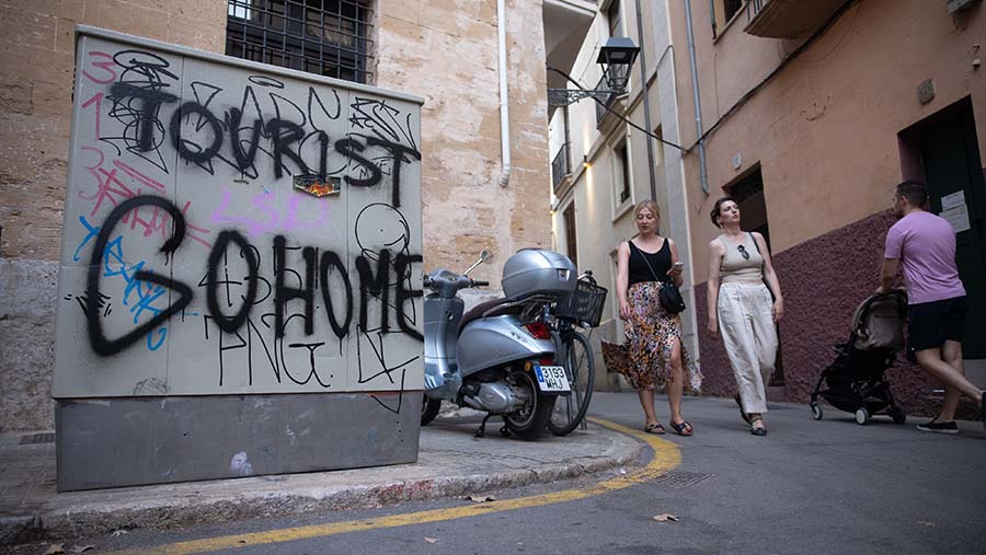 Turis melewati tulisan 'Tourist Go Home' terlihat di Palma de Mallorca, Spanyol, Jumat (26/7/2024). (Andrey Rudakov/Bloomberg)