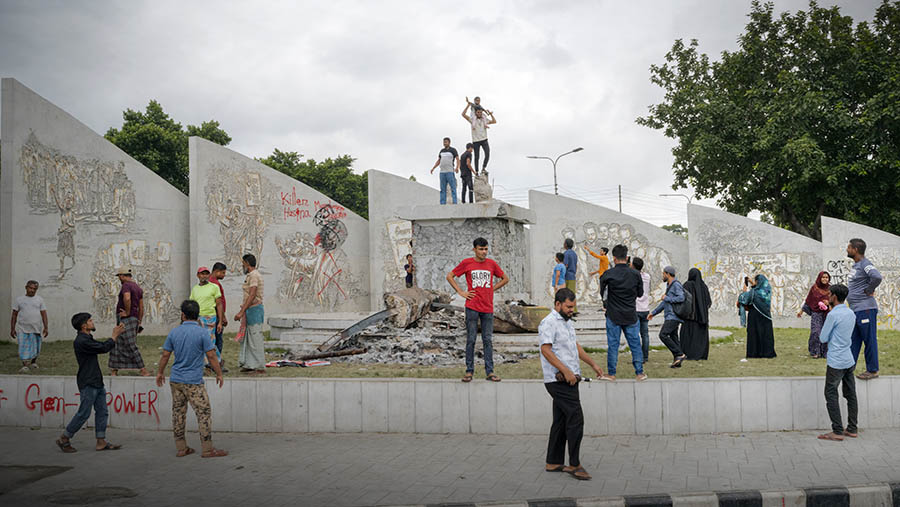 Pejalan kaki di depan tembok yang rusak setelah aksi protes di Dhaka, Bangladesh, Selasa (6/8/2024). (Fabeha Monir/Bloomberg)