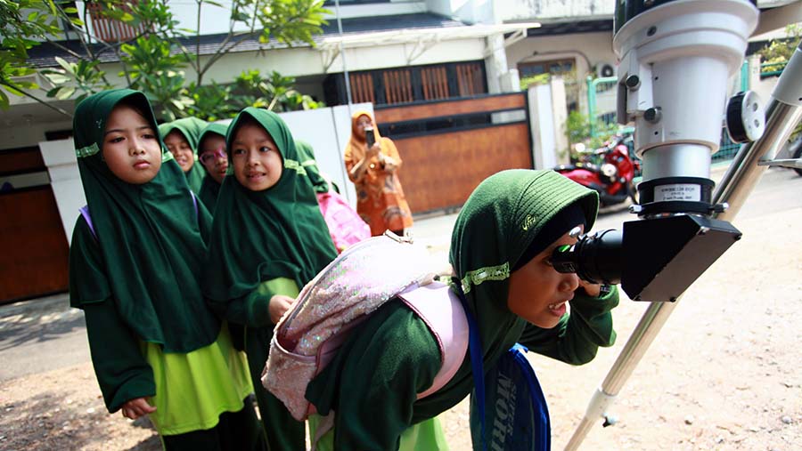 Siswa SD melihat bentuk matahari melalui teropong optik di MI Dakwah Islamiyah, Jakarta, Kamis (12/11/2024). (Bloomberg Technoz/Andrean Kristianto)