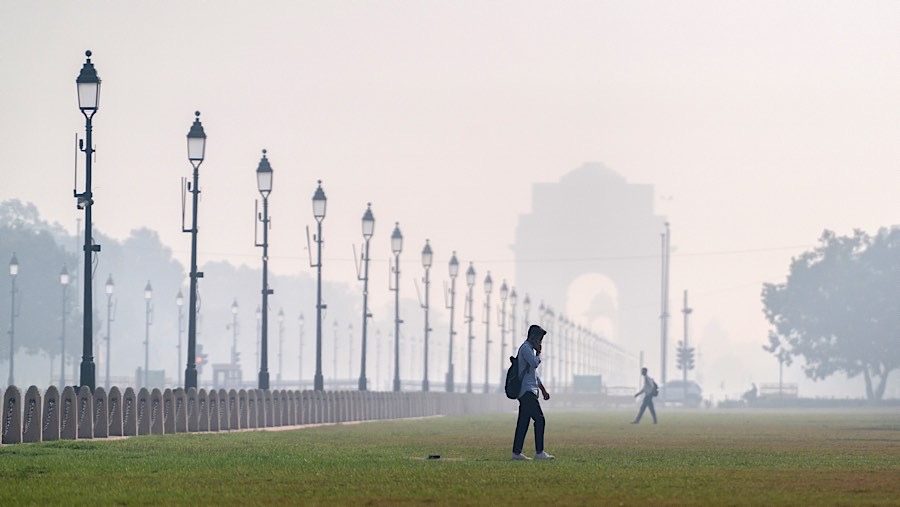 Pejalan kaki melewati Gerbang India yang diselimuti kabut asap polusi di New Delhi, India, Selasa (29/10/2024). (Anindito Mukherjee/Bloomberg)