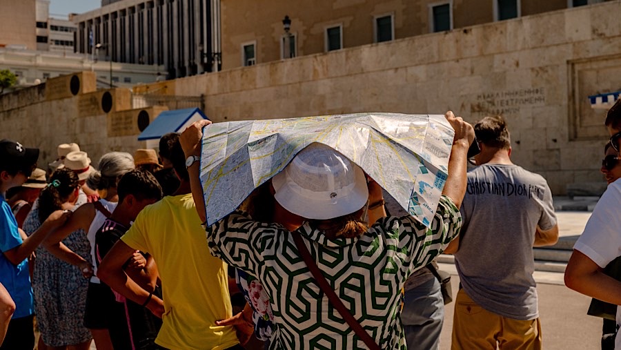 Warga melindungi wajahnya dari terik matahari saat suhu tinggi di Lapangan Syntagma di Athena, Yunani, Kamia (18/7/2024). (Hilary Swift/Bloomberg)