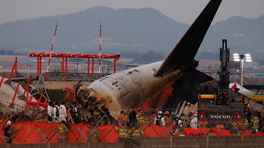 Petugas di depan reruntuhan pesawat Jeju Air Co. di Bandara Internasional Muan, Korea Selatan, Minggu (29/12/2024). (SeongJoon Cho/Bloomberg)
