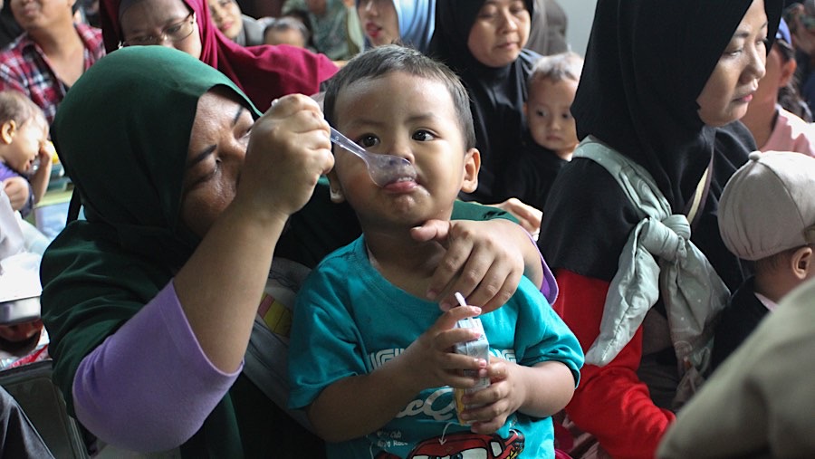 Seorang ibu menyuapi makan bergizi gratis (MBG) ke anaknya di Posyandu Dahlia 2, Ciracas, Jumat (10/1/2025). (Bloomberg Technoz/Andrean Kristianto)