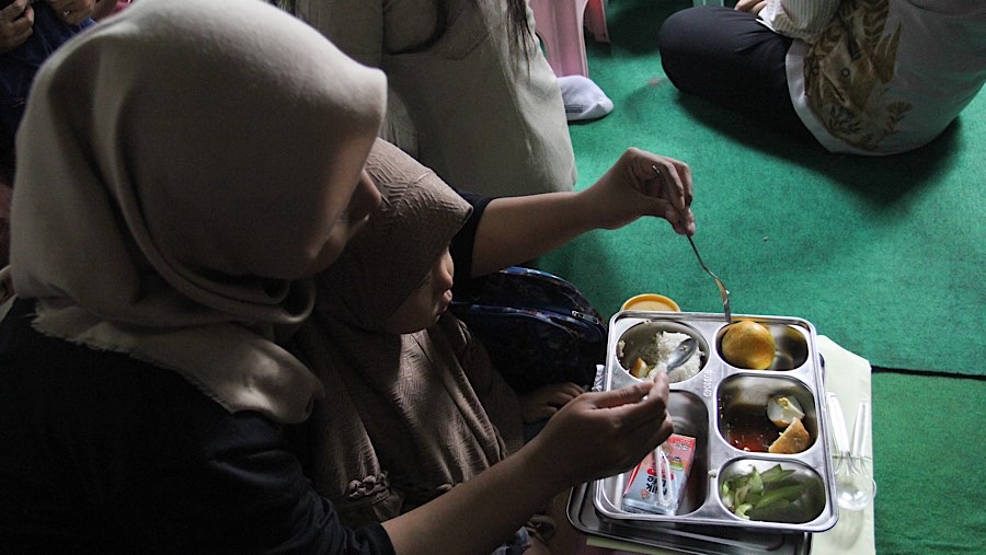 Seorang ibu dan anak menyantap makan bergizi gratis (MBG) di Posyandu Dahlia 2, Ciracas, Jumat (10/1/2025). (Bloomberg Technoz/Andrean Kristianto)