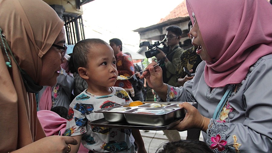 Seorang ibu menyuapi makan bergizi gratis (MBG) ke anaknya di Posyandu Anyelir 1, Ciracas, Jumat (10/1/2025). (Bloomberg Technoz/Andrean Kristianto)