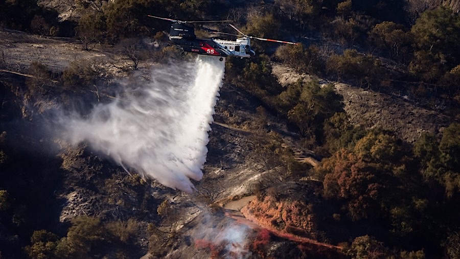 Helikopter menyiramkan air ke titik-titik api selama Kebakaran Palisades di Los Angeles, California, AS, Minggu (12/1/2025). (Kyle Grillot/Bloomberg)