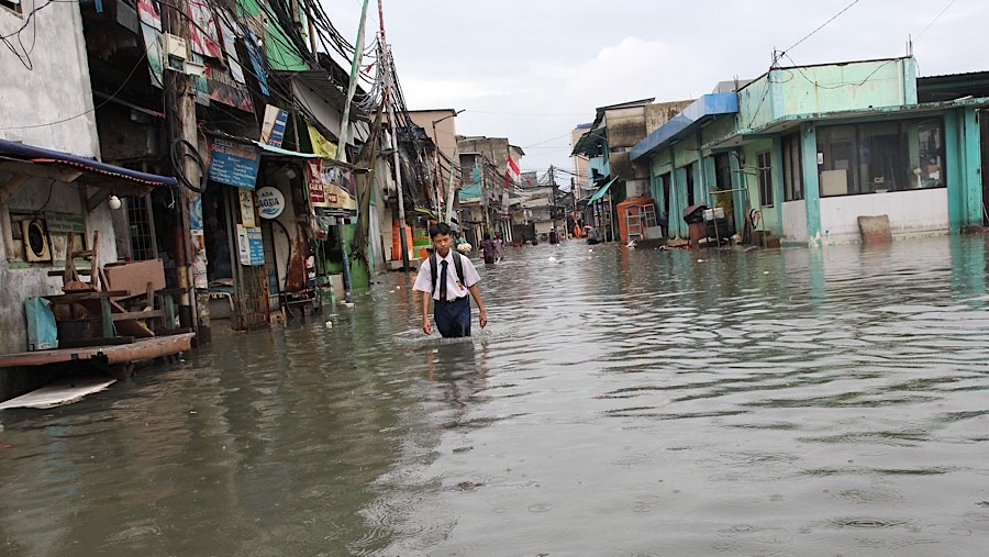 Anak sekolah melintasi banjir rob di Muara Angke, Penjaringan, Jakarta Utara, Selasa (14/1/2025). (Bloomberg Technoz/Andrean Kristianto)