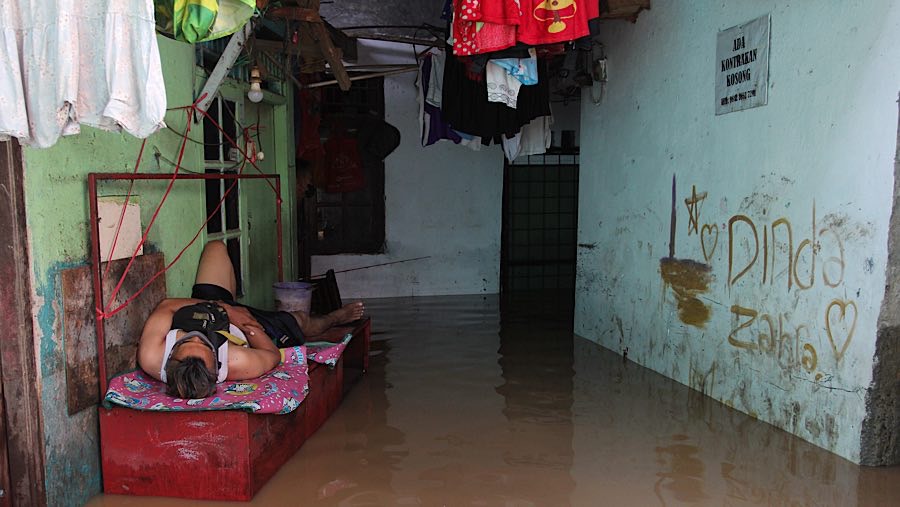 Warga memanfaatkan meja untuk tidur karena rumahnya terendam banjir. (Bloomberg Technoz/Andrean Kristianto)