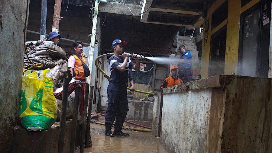 Pembersihan lumpur dibantu petugas pemadam kebakaran yang menyemprotkan air ke rumah warga. (Bloomberg Technoz/Andrean Kristianto)