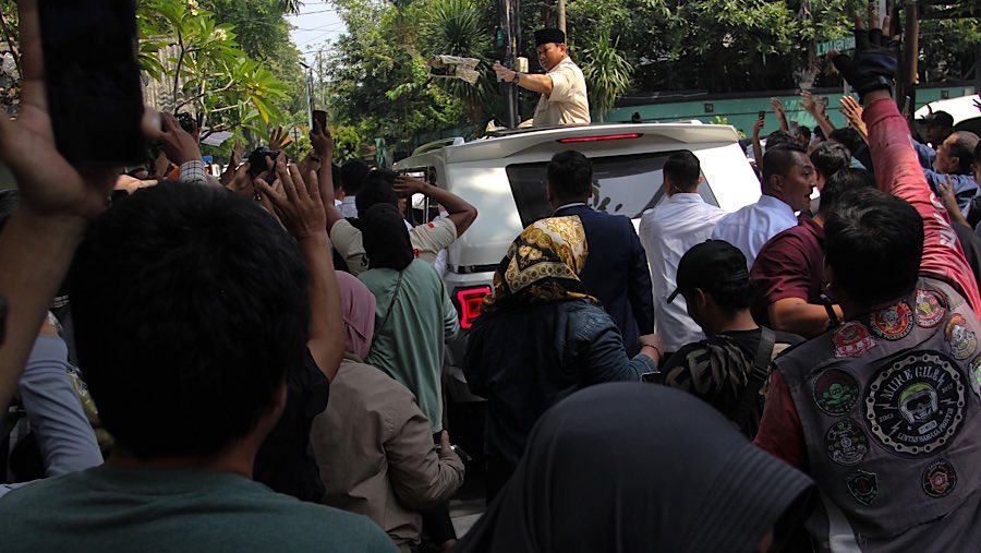 Presiden Prabowo Subianto juga menbagikan kaus ke warga dari atas mobilnya. (Bloomberg Technoz/Andrean Kristianto)