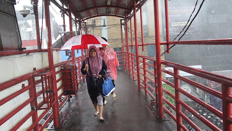 Warga menggunakan payung berjalan saat hujan lebat di JPO Mampang, Jakarta, Selasa (3/6/2025). (Bloomberg Technoz/Andrean Kristianto)