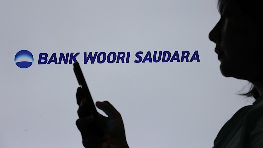 Warga menggunakan gawai dengan latar logo Bank Woori Saudara di Jakarta, Selasa (10/4/2025). (Bloomberg Technoz/Andrean Kristianto)