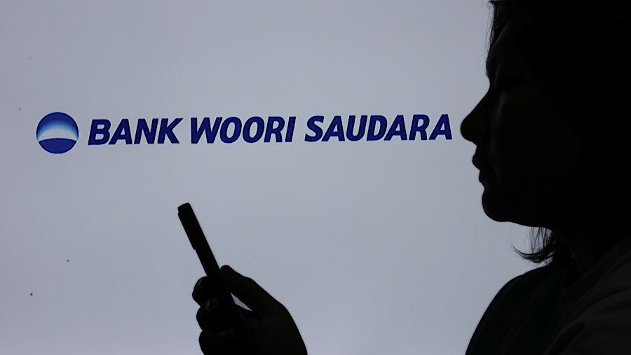 Warga menggunakan gawai dengan latar logo Bank Woori Saudara di Jakarta, Selasa (10/4/2025). (Bloomberg Technoz/Andrean Kristianto)
