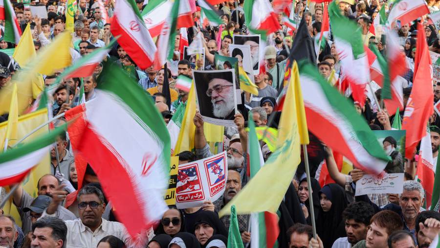 Warga Iran membentangkan bendera negara dan poster Ayatollah Ali Khamenei. (Bloomberg)