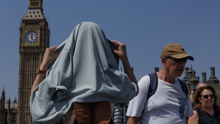 Perempuan menutup kepala dari terpaan sinar di Jembatan Westminster, London, Inggris. (Bloomberg)
