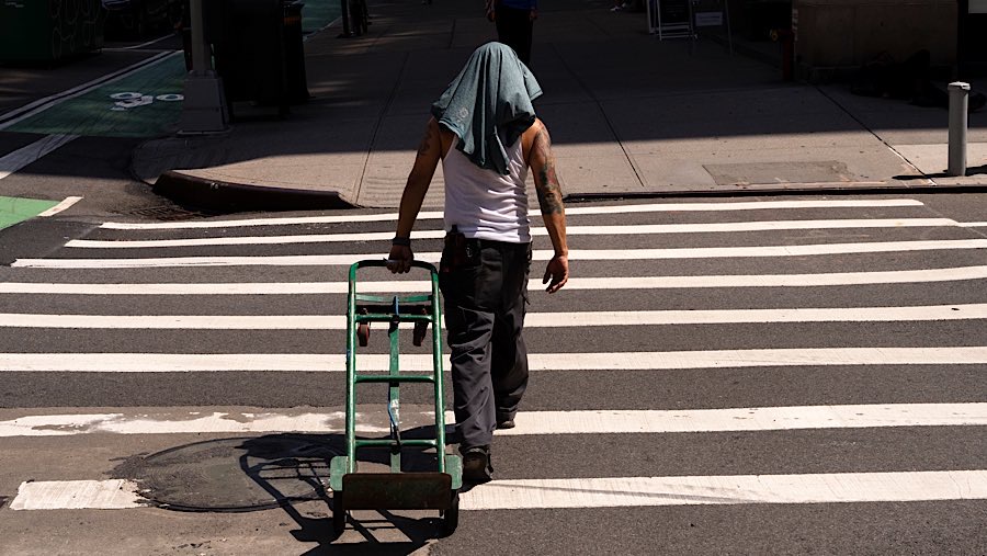 Pekerja menutupi kepalanya dengan kaus oblong saat suhu tinggi di New York, AS, Senin (23/6/2025). (Adam Gray/Bloomberg)