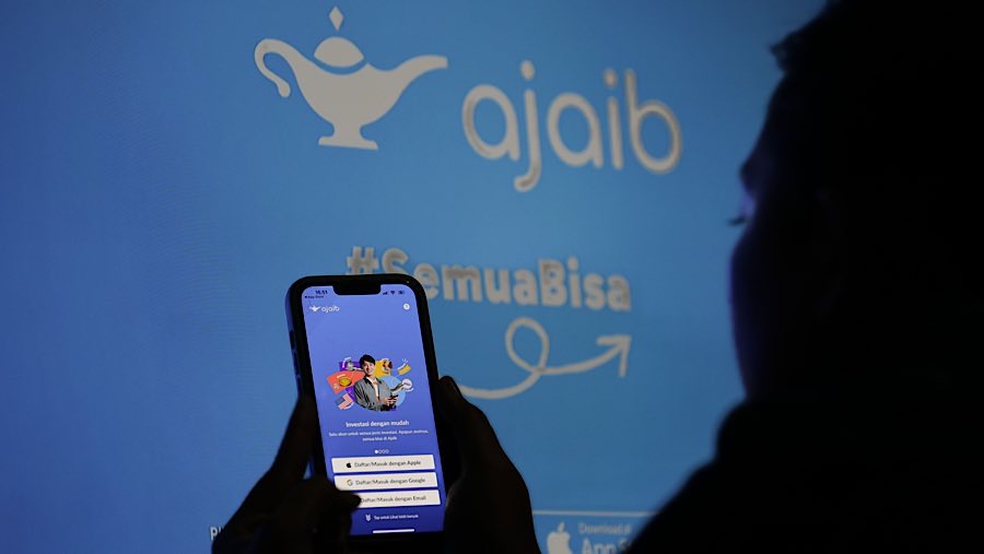 Warga menggunakan gawai dengan latar logo Ajaib Sekuritas di Jakarta, Selasa (1/7/2025). (Bloomberg Technoz/Andrean Kristianto)