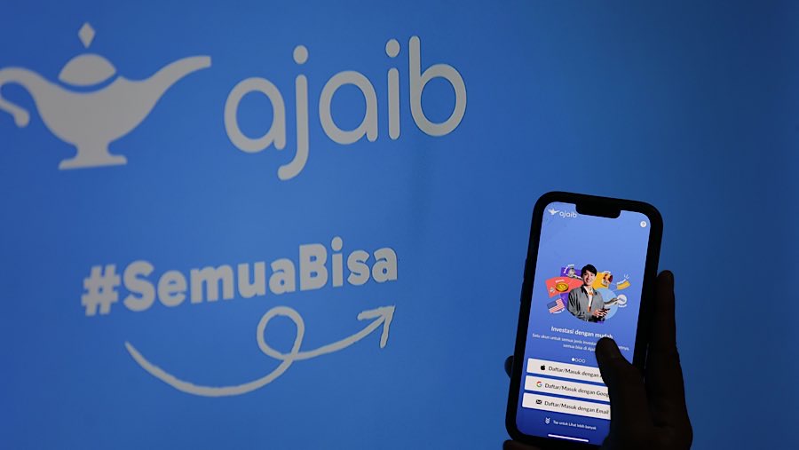 Warga menggunakan gawai dengan latar logo Ajaib Sekuritas di Jakarta, Selasa (1/7/2025). (Bloomberg Technoz/Andrean Kristianto)