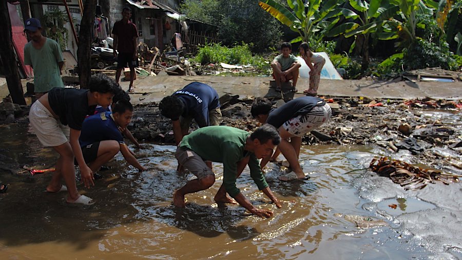 Beberapa warga terlihat mencari ikan saat genangan air yang melanda permukiman mereka. (Bloomberg Technoz/Andrean)